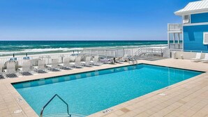 Ein Poolbereich mit Blick auf das Meer, Liegestühle und ein Gebäude mit Balkon.