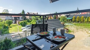 Un balcón con una mesa lista para el desayuno, con vistas a un área residencial con casas y árboles.