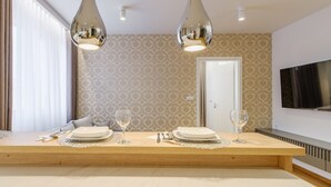 Un comedor moderno con una mesa de madera preparada para cuatro personas, dos lámparas colgantes y un televisor en la pared.