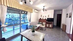 Una sala de estar con un ventanal grande, televisor, sofá, mesa de centro y una mesita con una planta.
