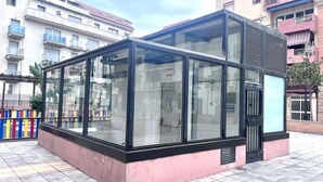 Un moderno edificio con paredes de vidrio y base rosada, rodeado de edificios residenciales de varios pisos.