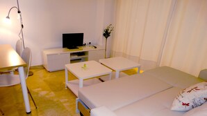 Ein Hotelzimmer mit einem Bett, zwei Nachttischen, einem Schreibtisch mit Stuhl, einem Fernseher und einer kleinen Pflanze.