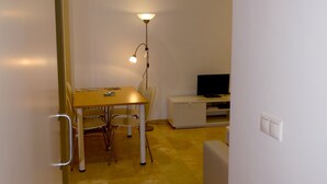 Ein gemütlicher Wohnraum mit Esstisch, Stühlen, einem kleinen Fernseher auf einem Schrank und einer Stehlampe.
