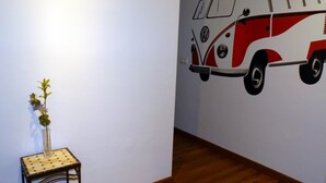 A room with a wooden floor, a small table with a vase of flowers, and a wall mural of a red and white van. - Minimalist center loft (Córdoba)