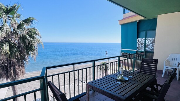 A balcony with a wooden table, chairs, and a view of the beach and ocean. - Costa del Sol apartment. (Fuengirola)
