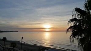 A beach view with a sunset, a building with outdoor seating, and palm trees. - Costa del Sol apartment. (Fuengirola)