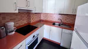 A compact kitchen with white cabinets, a red countertop, a sink, a stove, and a dishwasher. - Costa del Sol apartment. (Fuengirola)