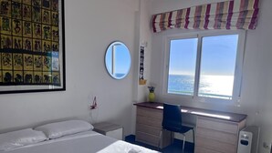 A hotel room with a bed, a desk, a chair, a large window with a view of the sea, a round mirror, and a wall with artwork. - Costa del Sol apartment. (Fuengirola)