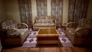 A cozy living room with a sofa and two armchairs, a wooden coffee table, patterned curtains, and a woven rug.