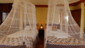 Two beds with mosquito nets, a nightstand with a lantern, and wooden walls.