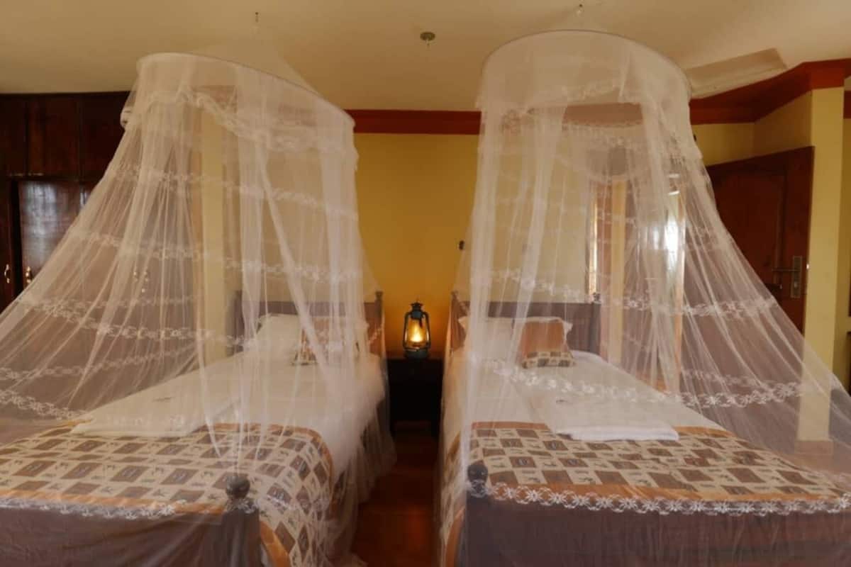 Two beds with mosquito nets, a nightstand with a lantern, and wooden walls.