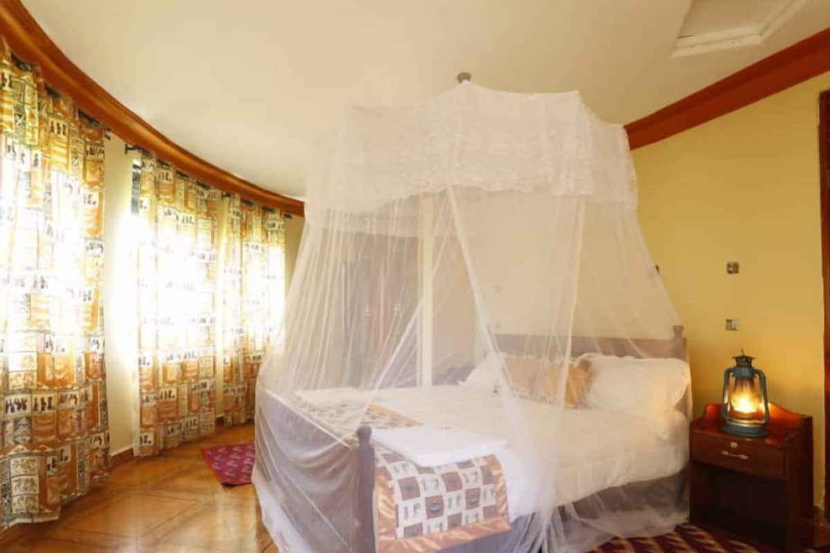 A bed with a canopy, a nightstand with a lantern, patterned curtains, and a patterned rug.