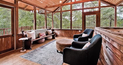 Escape to Whispering Hollow, a peaceful retreat near Eureka Springs with a dreamy glass room, cozy indoor spaces, and a brand-new hot tub for unwinding under the trees and surrounded by nature.