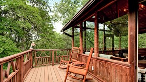 Une terrasse en bois, agrémentée de fauteuils à bascule et d’une table, entourée d’arbres.