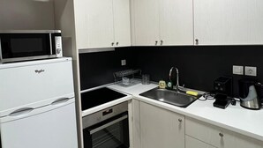 Ett kompakt kök med vita skåp, en mikrovågsugn, en spis och ett handfat.