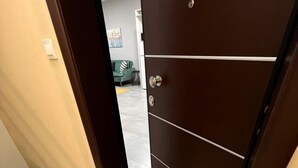 En hall med en brun dörr, en dörrmatta med ordet ”aloha” skrivet på den, och en liten inblick i ett vardagsrum med en grön soffa och en tavla på väggen.