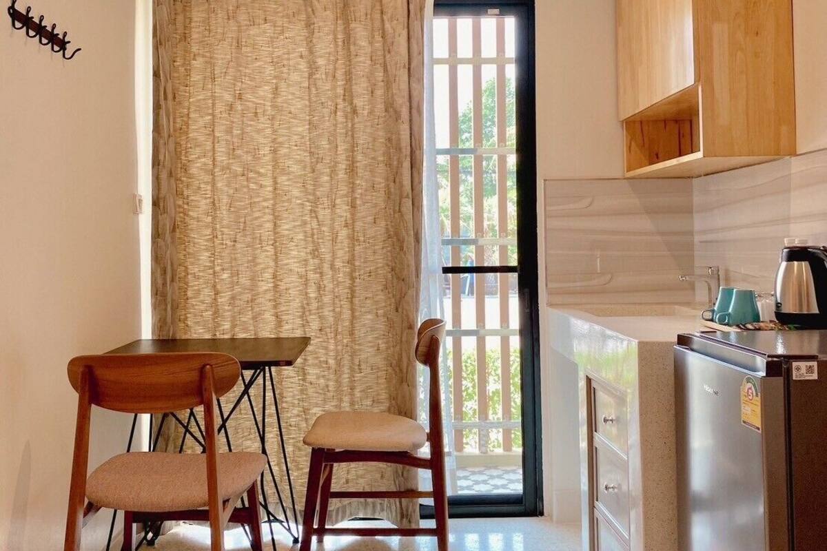 A compact kitchen with a dining area, a refrigerator, and a window with curtains.