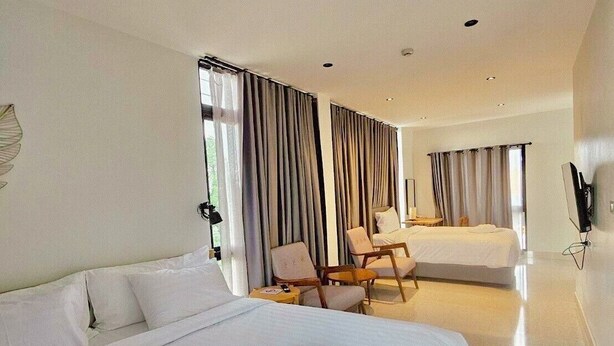 A modern hotel room with a large bed, a smaller bed, a ceiling fan, and a seating area with chairs. - Calamint Residence Hotel  (Chumphon)
