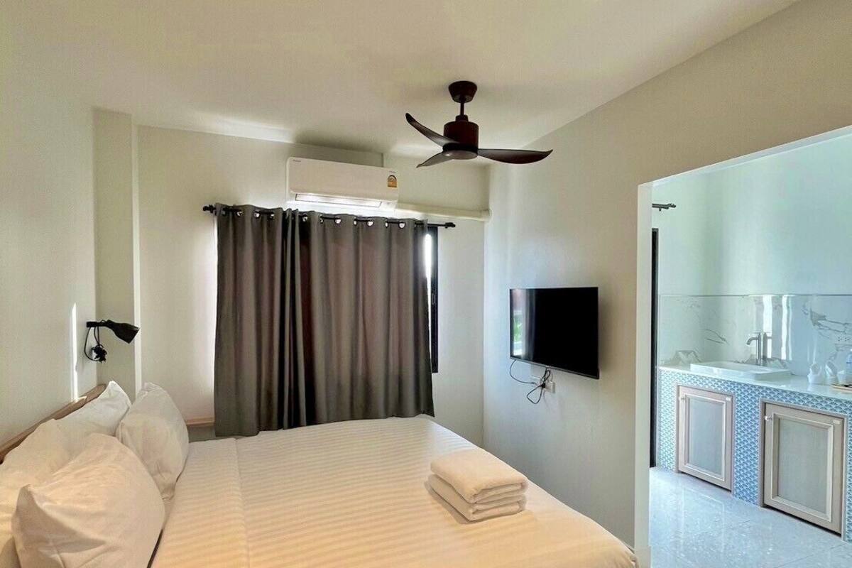 A hotel room with a bed, a ceiling fan, a flat-screen TV, a bathroom with a mirror, and a tiled floor.