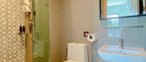 A modern bathroom with a glass-enclosed shower, a toilet, a sink, and a trash bin.