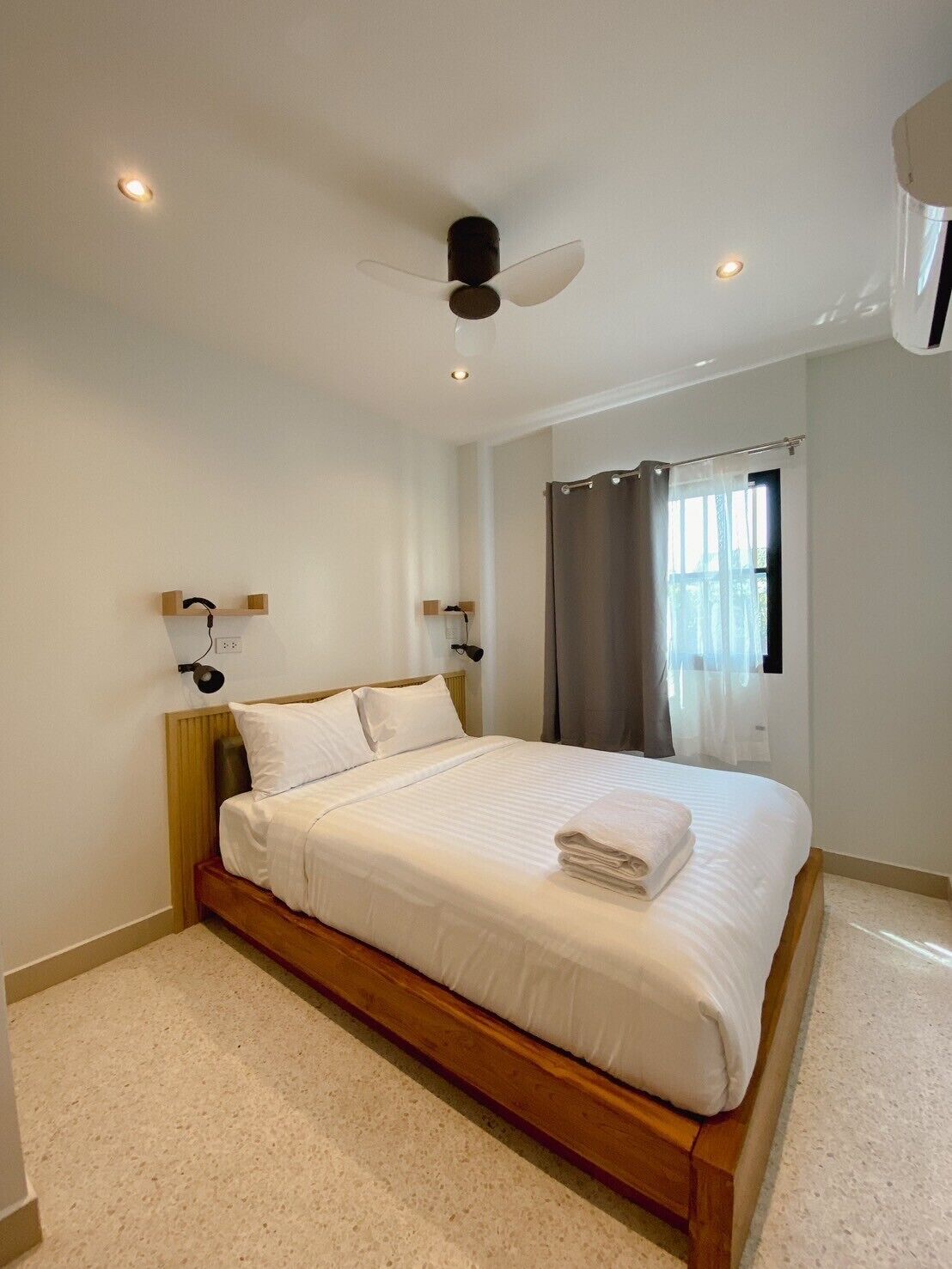 Un dormitorio con cama, ventilador de techo, ventana con cortinas y lámpara de pared.