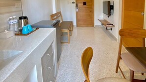 A compact kitchen with a countertop, wooden cabinets, a ceiling fan, and a dining area with a table and chairs. - Calamint Residence Hotel  (Chumphon)