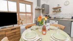 A dining area with a table set for four, a television, and a kitchen in the background.
