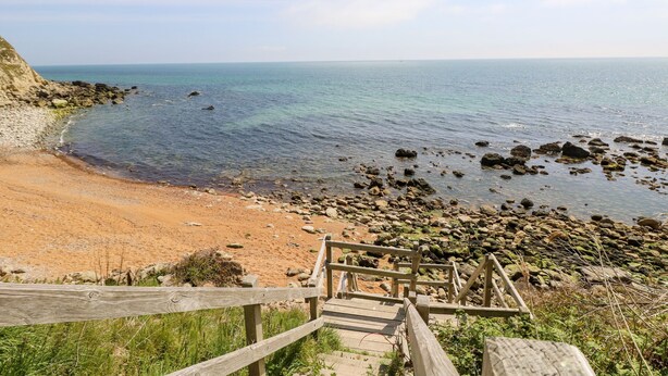 A wooden staircase leading to a beach with clear blue water and rocky shore.