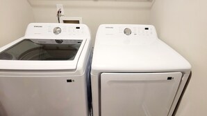 Deux lave-linge Samsung à chargement frontal, de couleur blanche, se trouvent dans une buanderie avec un mur blanc et une prise de courant au-dessus.