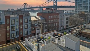 A rooftop patio with outdoor seating, overlooking a cityscape and a bridge.