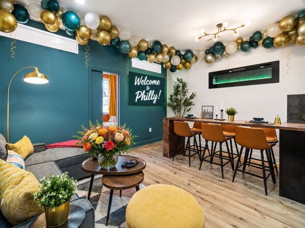 A modern living room with a sofa, a coffee table with a floral arrangement, and a dining area with a bar.