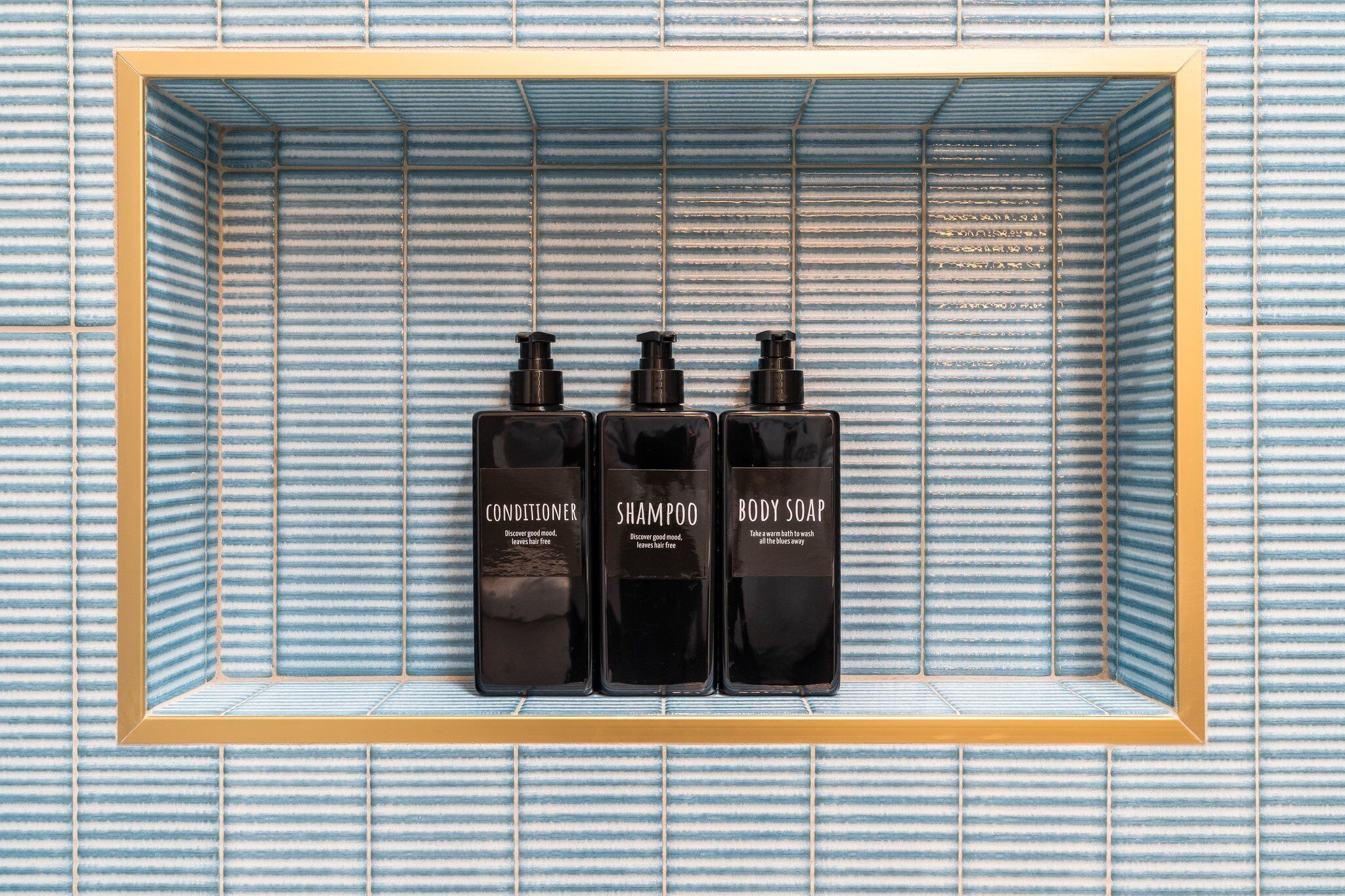 A shelf with three bottles of toiletries: conditioner, shampoo, and body soap.