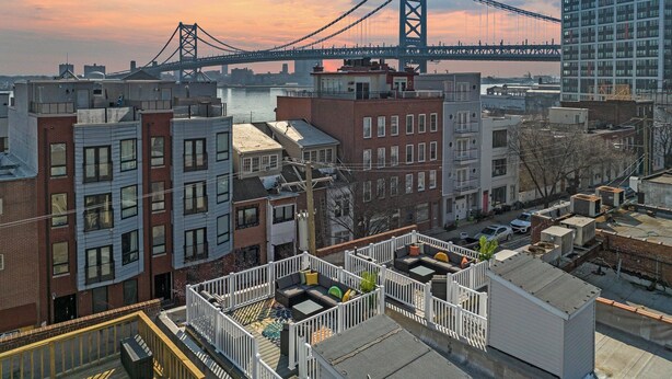 A rooftop patio with outdoor seating, overlooking a cityscape and a bridge.