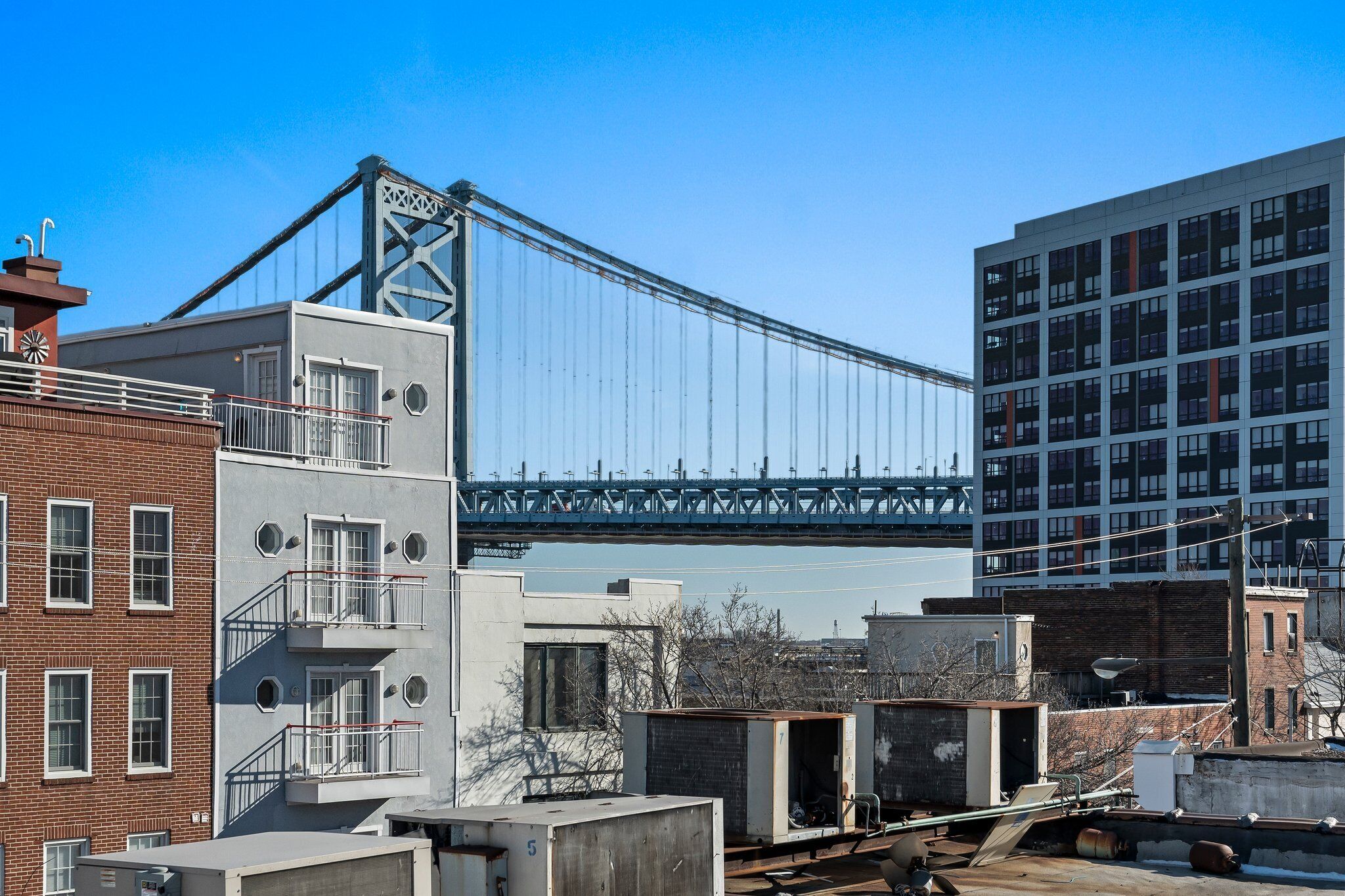 A modern building with a large glass facade, a prominent bridge in the background, and a mix of brick and concrete structures nearby.