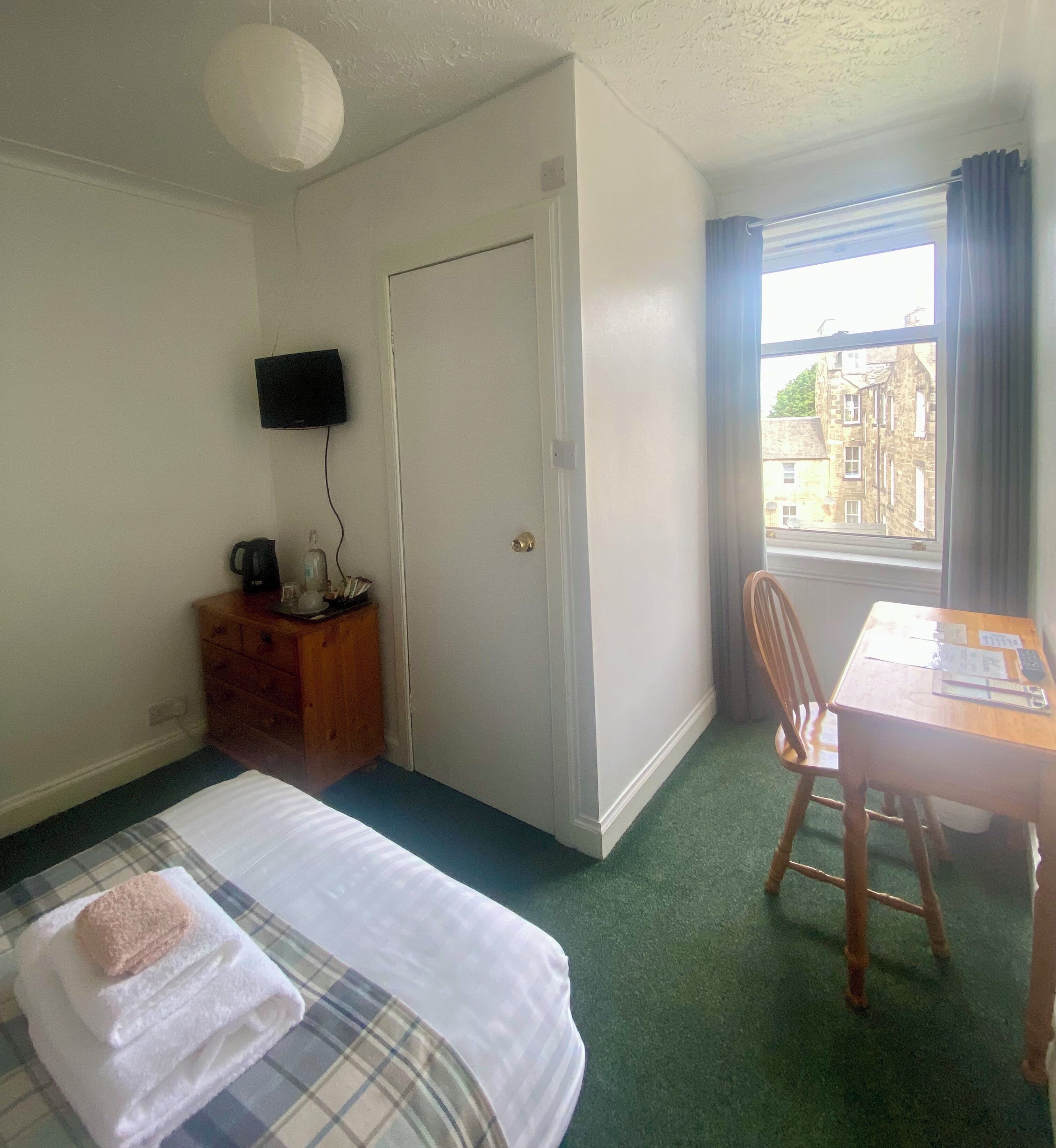 Ein Hotelzimmer mit Bett, Schreibtisch, Stuhl, Fernseher und einem Fenster mit Blick auf Gebäude.