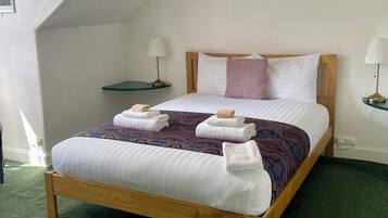 A neatly made bed with white linens and a purple blanket, two bedside tables with lamps, and a green carpeted floor.