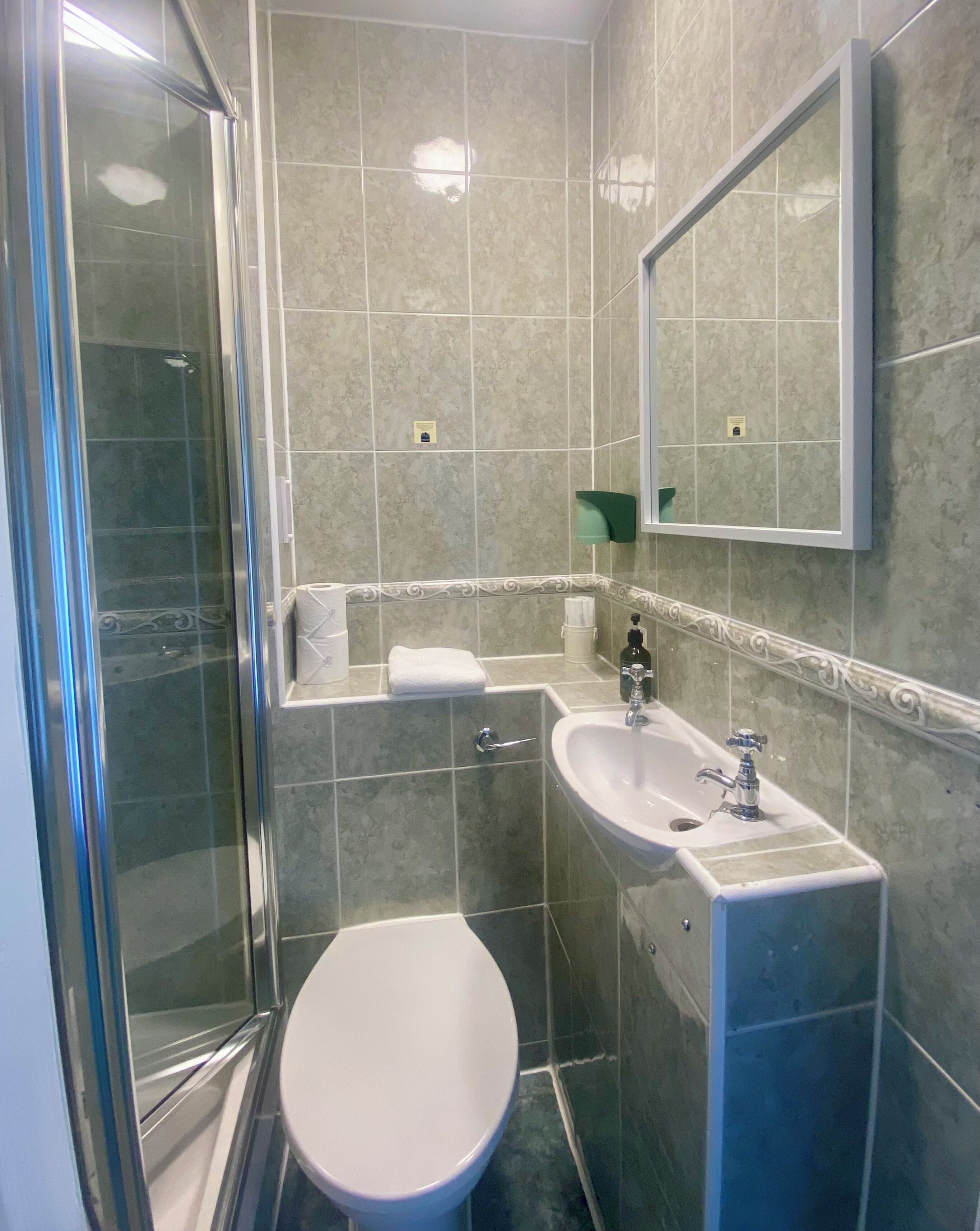 A bathroom with a glass shower enclosure, a white toilet, a sink with a mirror above it, and a towel on the counter.