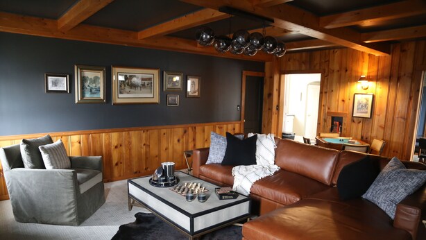 A cozy living room with a brown leather sofa, a grey armchair, and a coffee table with chess pieces. - Lena's Place (Findlay)