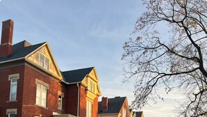 A row of red brick townhouses with a front porch, a sidewalk, and a grassy area with fallen leaves. - Lena's Place (Findlay)