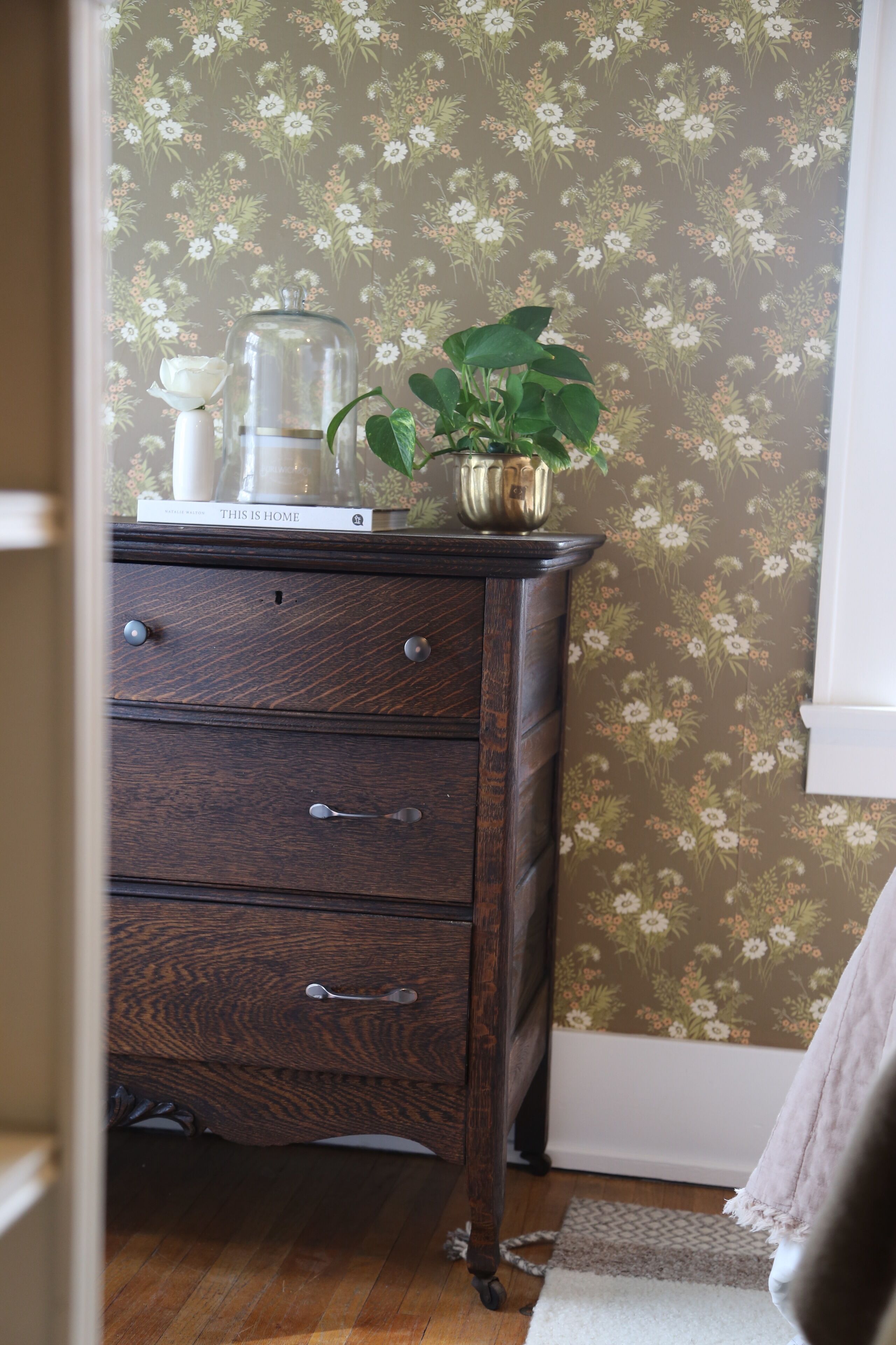 A wooden dresser with drawers, a glass jar, a white vase, and a potted plant.