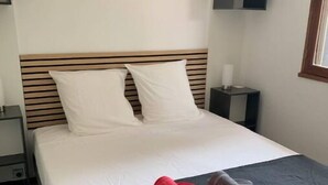 A hotel room with a bed, a nightstand, a lamp, and a window.