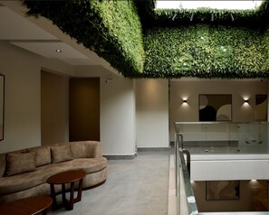 A modern interior with a green wall, a sofa, a small table, and a glass railing. - Micassa Residences and Suites (Kampala)