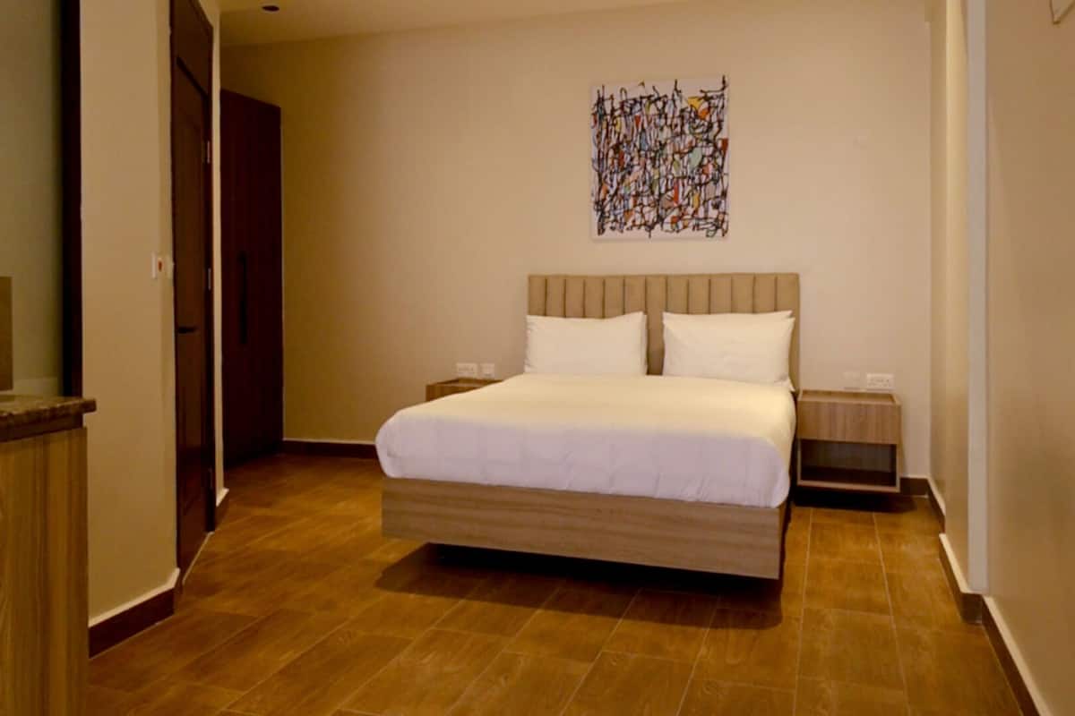 A bedroom with a bed, a nightstand, a wall art piece, and a wooden floor.