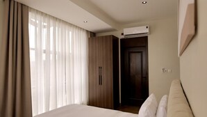 Una habitación de hotel con una cama grande, un armario, un equipo de aire acondicionado y una puerta.