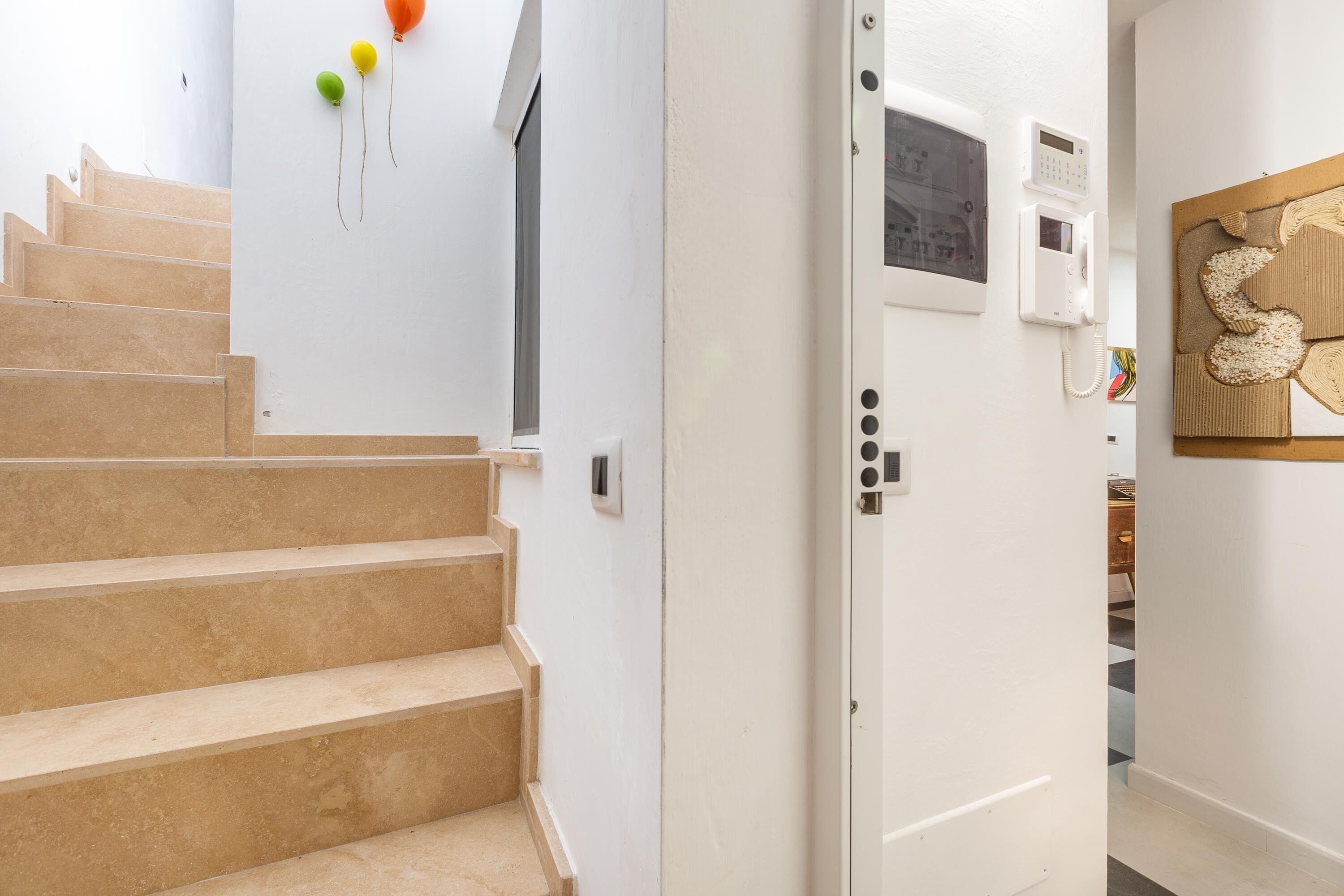 A staircase leading to a room with a white door, a wall-mounted intercom, and a decorative wall piece.