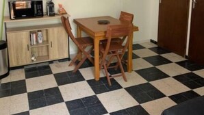 Een kleine, schone kamer met een zwart-wit betegelde vloer, een houten tafel met stoelen, een magnetron, een koffiezetapparaat en een televisie aan de muur.