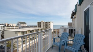 Un balcon avec deux chaises bleues, une balustrade blanche et une vue sur l’océan et les bâtiments en arrière-plan.