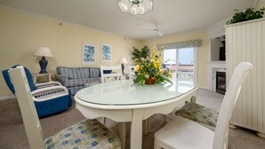 Un salon avec une table à plateau en verre, des chaises blanches, un canapé bleu et un meuble blanc.