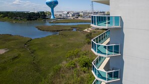 Ein modernes Gebäude mit einem Glasbalkon mit Blick auf ein Gewässer und einem markanten, blauen Turm im Hintergrund.