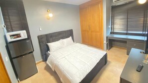 A bedroom with a bed, a desk, a wardrobe, a microwave, and an air conditioner. - Mulliner Towers (Lagos)